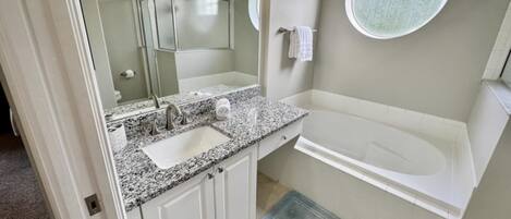Un baño con lavamanos de encimera de granito, un espejo grande, una bañera y un ventanal redondo.
