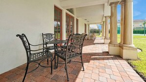 Eine überdachte Terrasse mit Backsteinboden, Metallstühlen und einem Tisch.