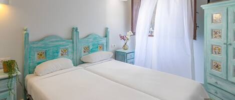 A bedroom with two beds, a nightstand, a dresser, and a window with curtains.