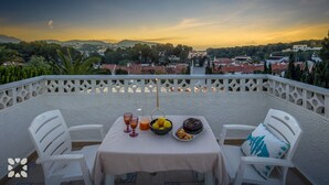 Eine Terrasse mit einem für zwei Personen gedecktem Tisch, mit Blick auf eine Stadtlandschaft bei Sonnenuntergang.