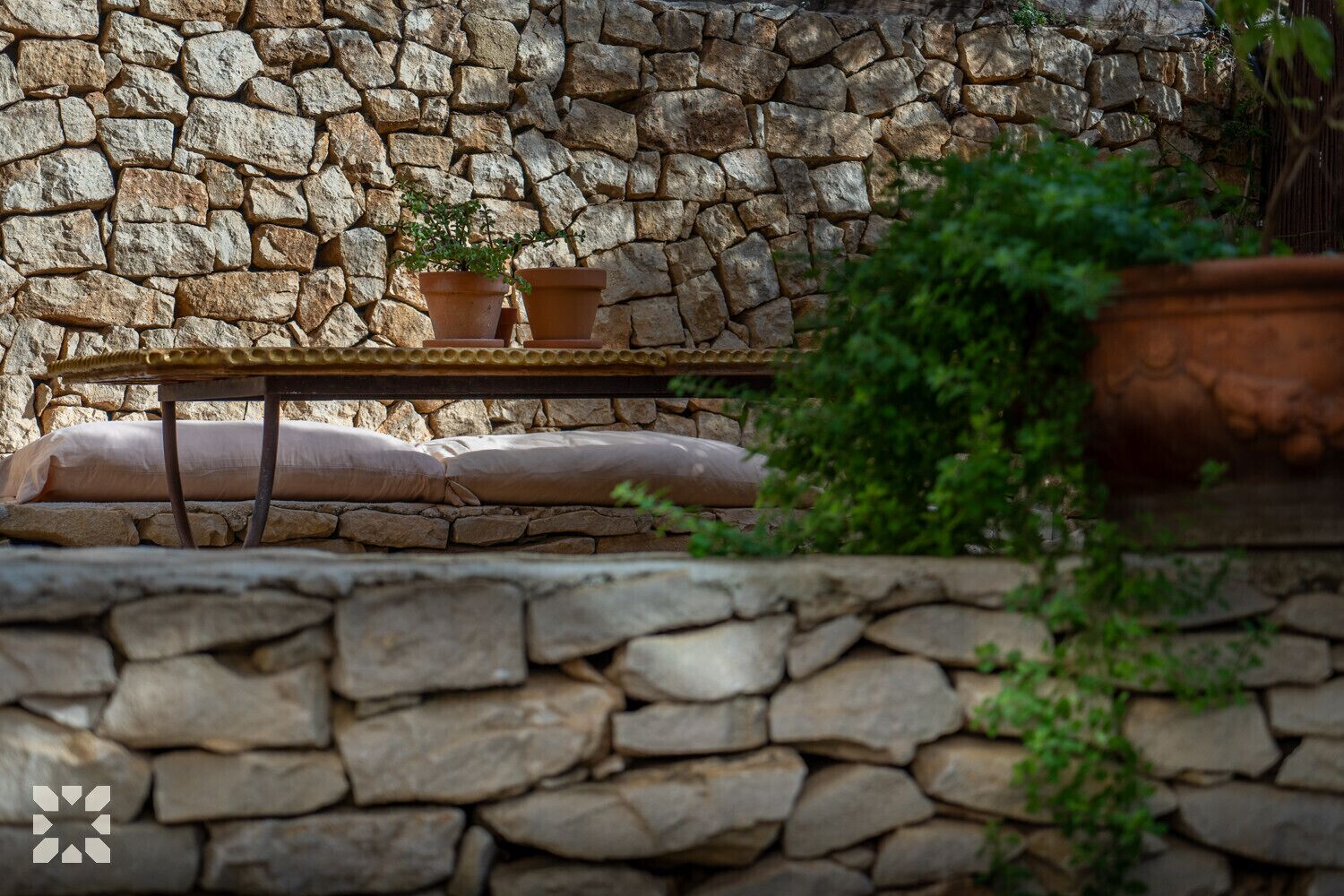 Un mur de pierres bordant un espace extérieur aménagé avec un style rustique, comprenant une table en métal et deux jardinières en terre cuite.