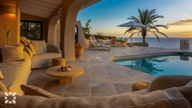 A poolside area with a sofa, lounge chairs, and a table with fruit.