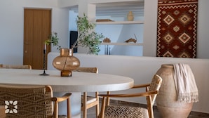 A round dining table with wicker chairs, a copper vase with a plant, and a woven basket.