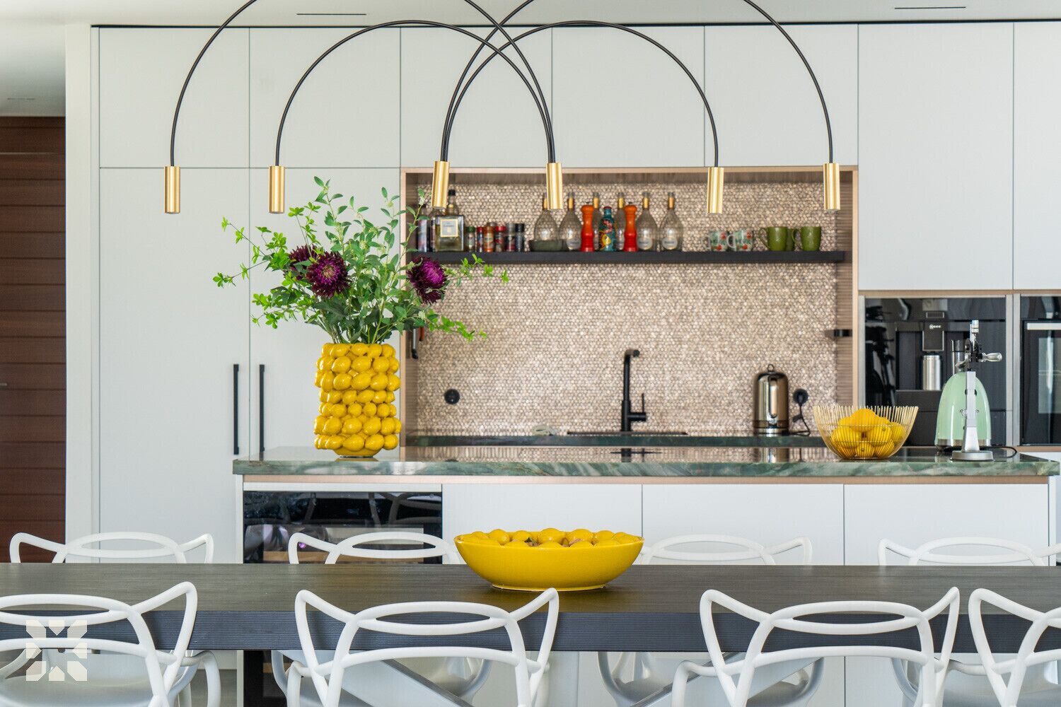 A modern kitchen with white cabinets, a central island with a yellow bowl, and a hanging light fixture.