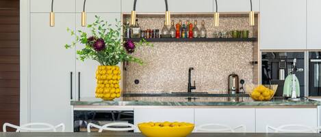 A modern kitchen with white cabinets, a central island with a yellow bowl, and a hanging light fixture.
