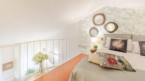 Ein Schlafzimmer mit einem Bett, einem Nachttisch, einem an der Wand befestigten Spiegel und einer Treppe.