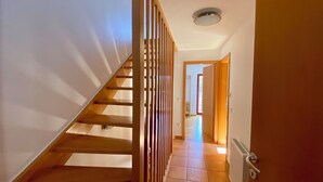 Un couloir avec un escalier en bois, un radiateur et une porte donnant sur une autre pièce.