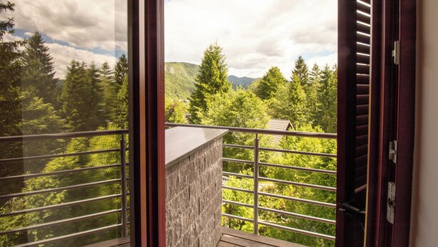 Un balcon doté d’un mur en pierre et d’une rambarde en métal, offrant une vue sur une région montagneuse boisée.