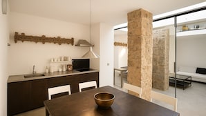 A modern kitchen with dark cabinetry, a dining table, and a large stone pillar. - dHomes -Loft suite in Duomo (Milan)