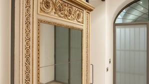 A room with a large ornate mirror, a sliding door, and a glass elevator door. - dHomes -Loft suite in Duomo (Milan)