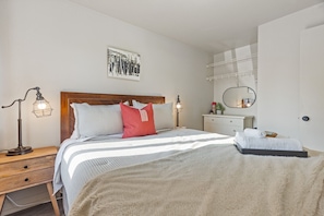 A neatly arranged bedroom with a bed, bedside lamps, a nightstand, a dresser, a mirror, and a framed picture on the wall.