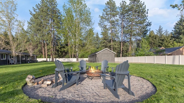 Un patio trasero con un brasero, cuatro sillas Adirondack y un cobertizo.