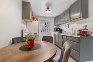 A kitchen with a wooden table, grey cabinets, a coffee machine, and a red plant in a can. - Family Friendly Space w/ Spacious Yard and Firepit (Columbia Falls)