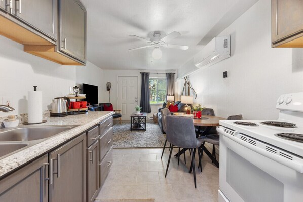 A modern kitchen with a dining area, granite countertops, stainless steel appliances, and a ceiling fan.