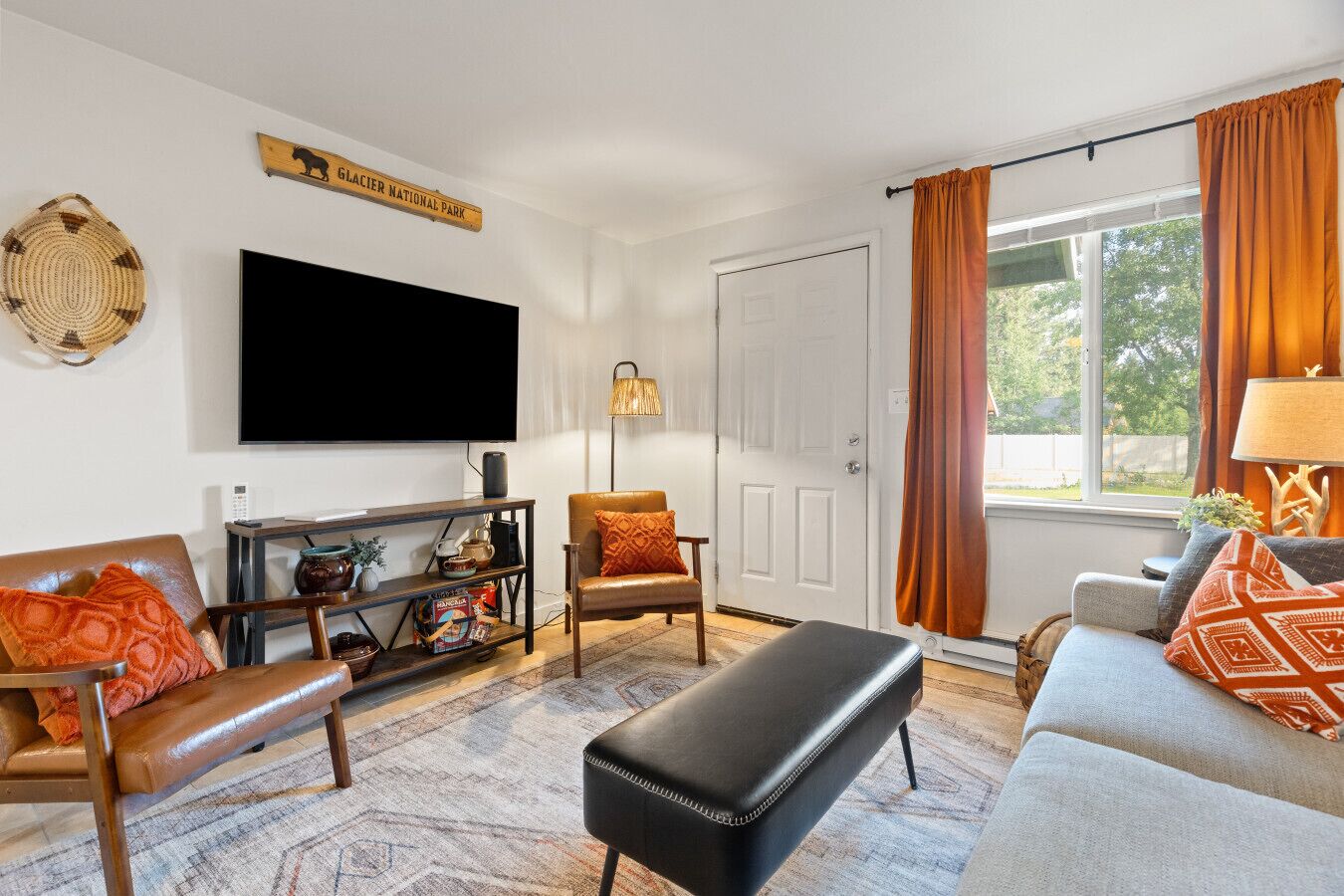 A living room with a flat-screen TV, leather sofas, a coffee table, a bookshelf, and a door with a sign above it.