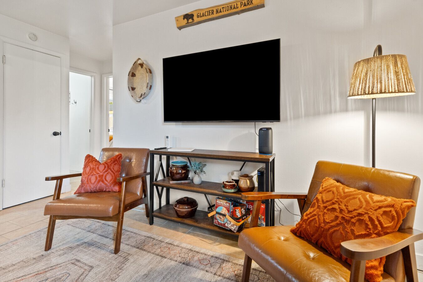 A living room with two leather chairs, a television, a lamp, and a shelf with decorative items.