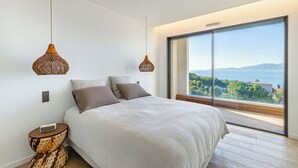 Quarto com uma cama grande, duas luminárias pendentes, uma mesa de cabeceira e vista para o mar.