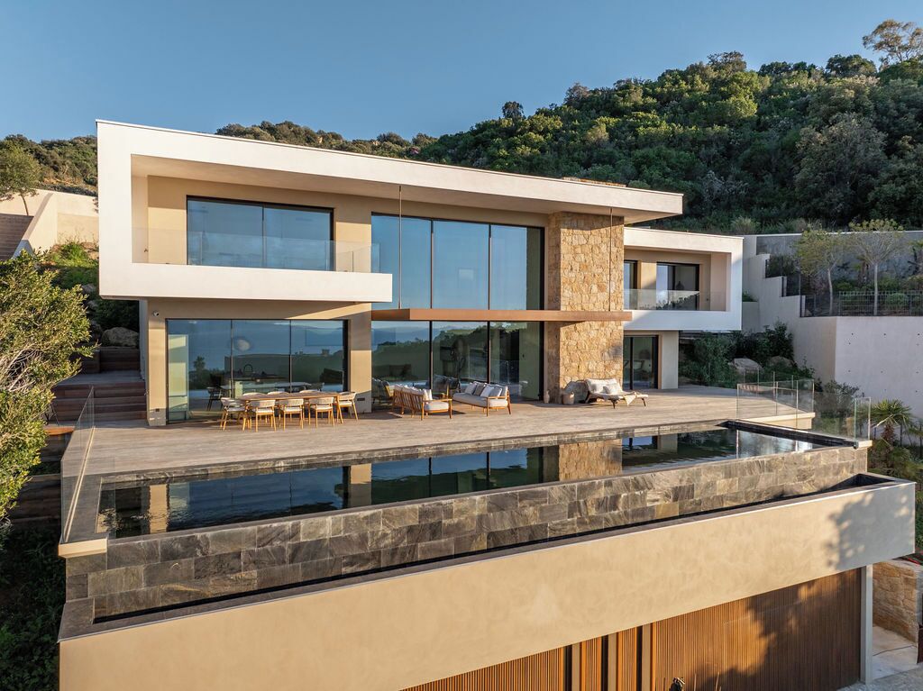 A modern two-story house with a glass-enclosed pool and outdoor seating area.