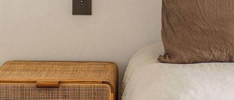 Une pièce avec une décoration murale en rotin tressé, une table de chevet, un lit avec un oreiller marron et un interrupteur fixé au mur.