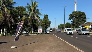 Une rue bordée de palmiers, une haute tour de télécommunications et un panneau indicateur.