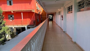 Un long couloir doté d’un sol carrelé, d’une balustrade blanche et d’un bâtiment rouge avec de nombreuses fenêtres et des unités de climatisation.