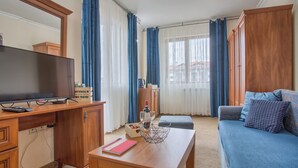A living room with a TV, wooden furniture, a blue sofa, and a window with curtains. - Charming 1-bedroom hotel suites in wonderful Bansko with WiFi (Bansko)