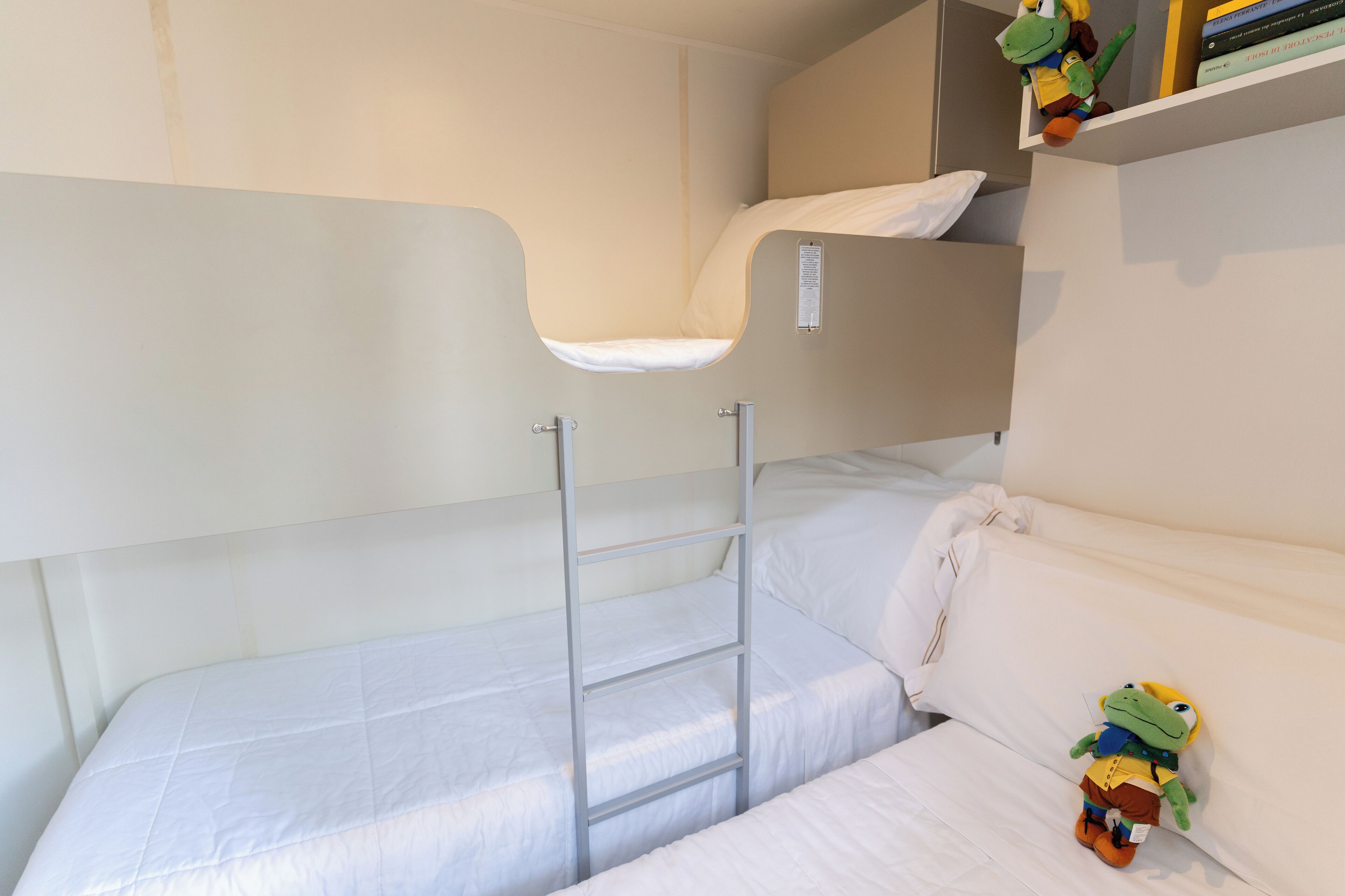 A bunk bed with a ladder, white bedding, and a small shelf with books and a toy.