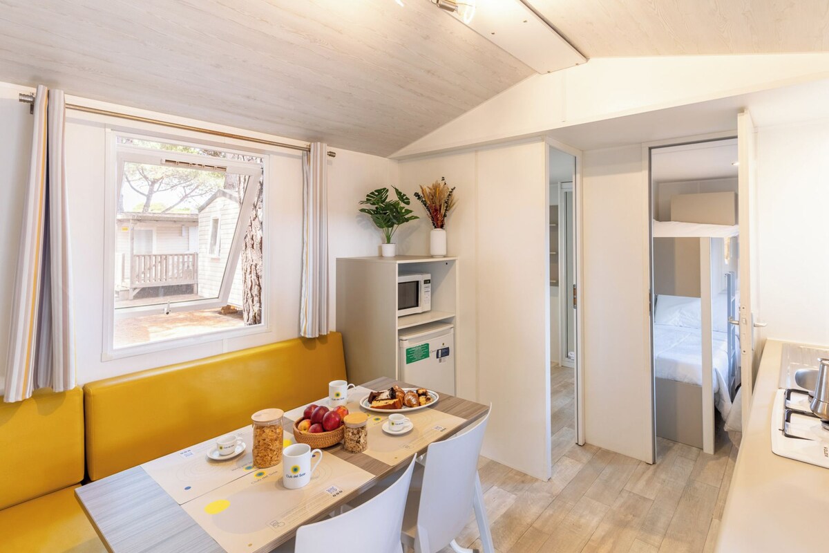 Une pièce compacte comprenant une table à manger, un banc jaune, un four à micro-ondes, un petit réfrigérateur et un lit dans la pièce adjacente.