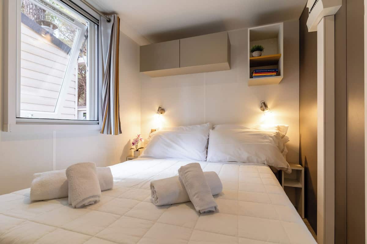 Habitación de hotel con una cama, dos lámparas de noche, un ventanal y una estantería empotrada con libros.