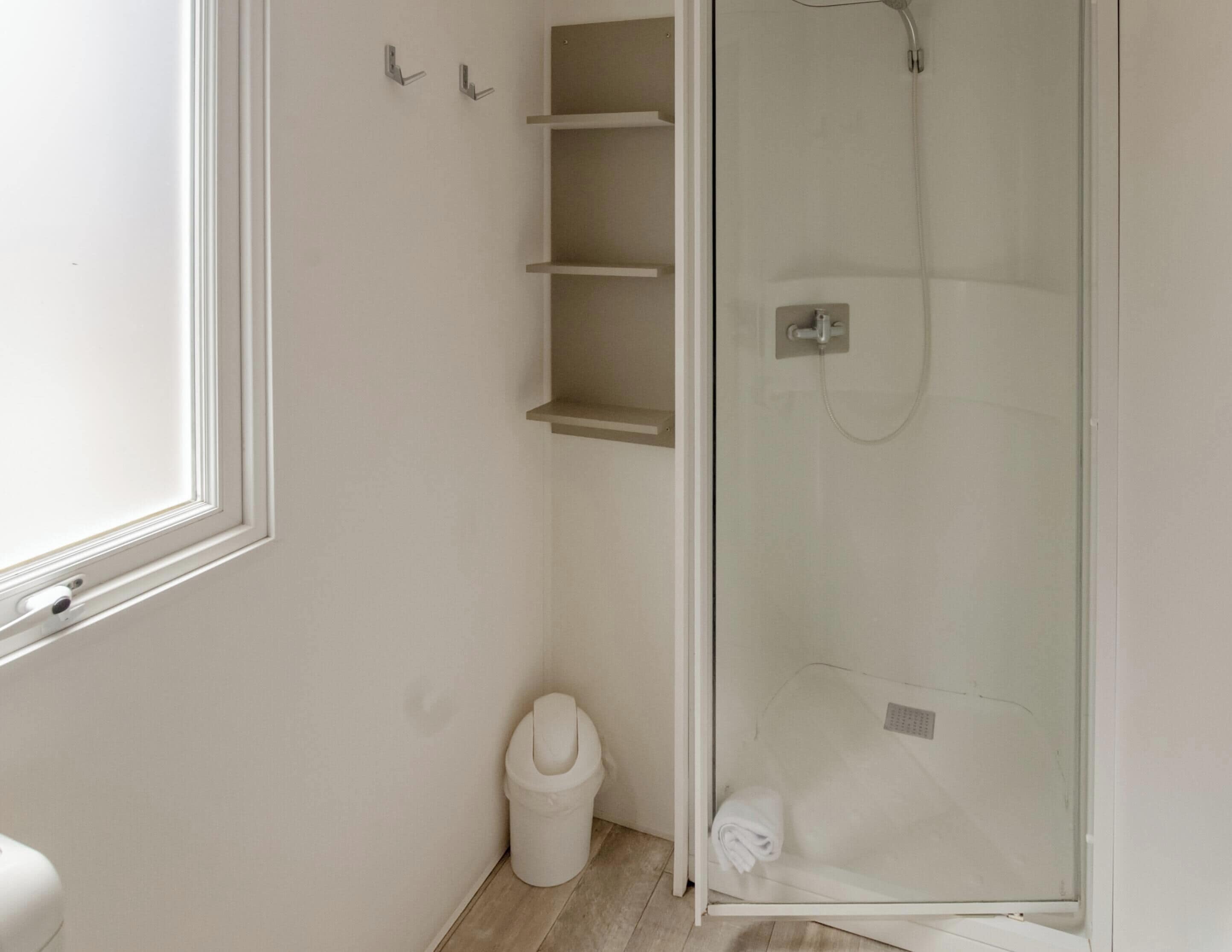 Un baño con inodoro, ducha con cerramiento de vidrio y ventana.
