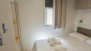 A hotel room with a bed, a window with curtains, a wardrobe, and a key on the floor. - Hotiday Lodge Orbetello (Orbetello)