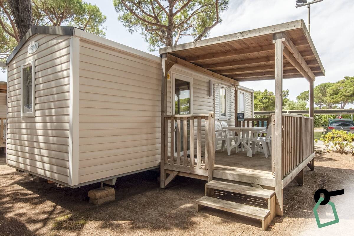 Una casa móvil con un porche de madera y una pequeña terraza, que incluye una mesa y sillas.