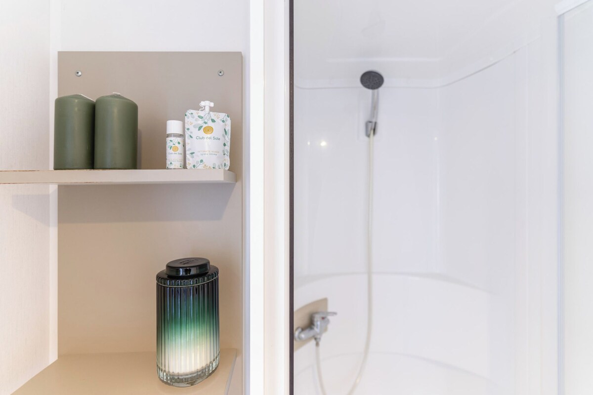 Un baño con ducha, un estante con artículos de aseo y una vela.