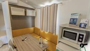 A compact room with a wooden table, a yellow cushioned bench, a microwave, and a small refrigerator. - Hotiday Lodge Orbetello (Orbetello)