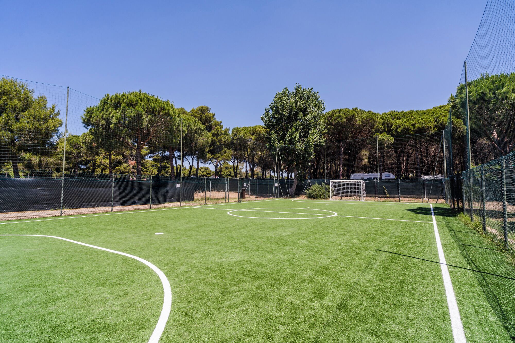 An outdoor soccer field with a goalpost, surrounded by a fence and trees.