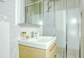 A modern bathroom with a white sink, a glass shower enclosure, and a mirror above the sink. - Le Chat Botté - Versailles (Versailles)