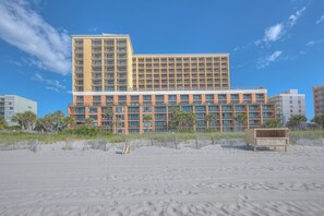Un hôtel à plusieurs étages, doté d’un toit plat, avec une plage de sable en premier plan.