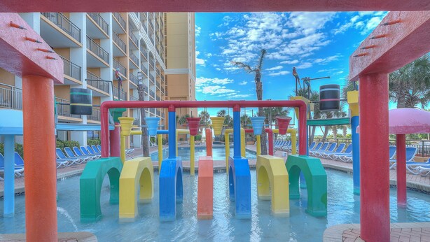 Ein Wassererlebnispark mit bunten Elementen und einem Pool im Hintergrund, mit Liegestühlen.