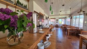 Een restaurant met een lange houten toonbank, een koffiemachine en een vaas met paarse bloemen.