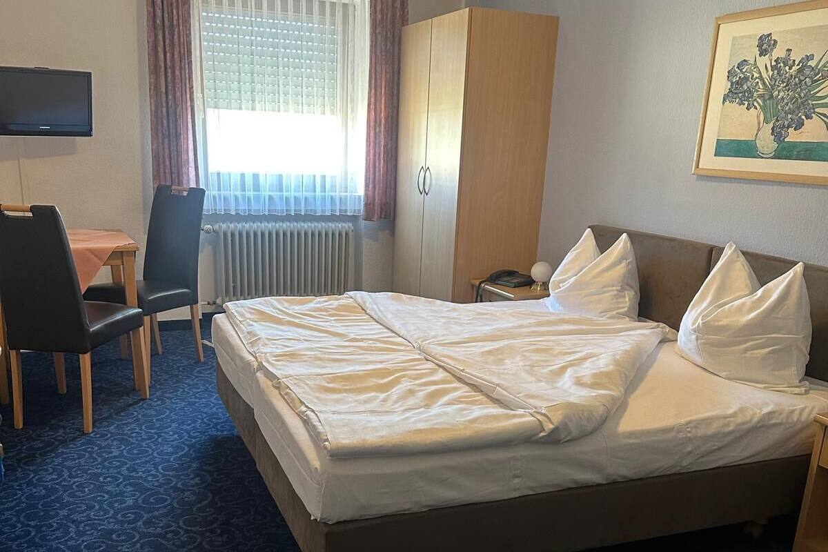 A hotel room with a bed, a desk, a chair, a wardrobe, and a painting on the wall.