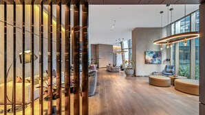Un vestíbulo moderno y espacioso con suelo de madera, una zona de estar central y grandes ventanales que dejan entrar mucha luz natural.