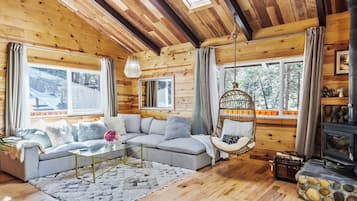 A cozy cabin interior with a sofa, hanging chair, and fireplace.