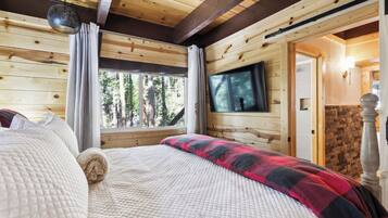 A wooden cabin bedroom with a bed, curtains, a TV, and a stone wall.