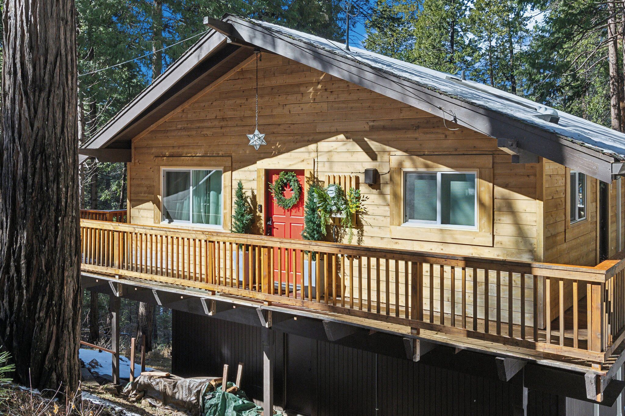 A wooden cabin with a balcony, a red door, and Christmas wreaths.