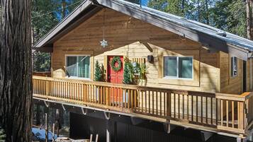 A wooden cabin with a balcony, a red door, and Christmas wreaths.