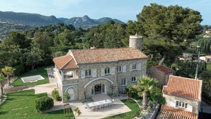 Una casa in pietra con tetto in tegole, un cortile centrale e una vista sulle montagne sullo sfondo.