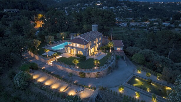 Una grande dimora in pietra con piscina, immersa in giardini rigogliosi e dotata di un viale ben illuminato.