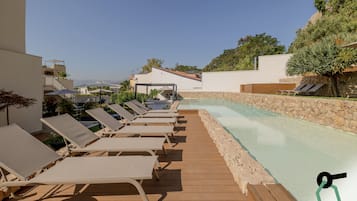 Una piscina al aire libre, sombrillas, sillones reclinables de piscina