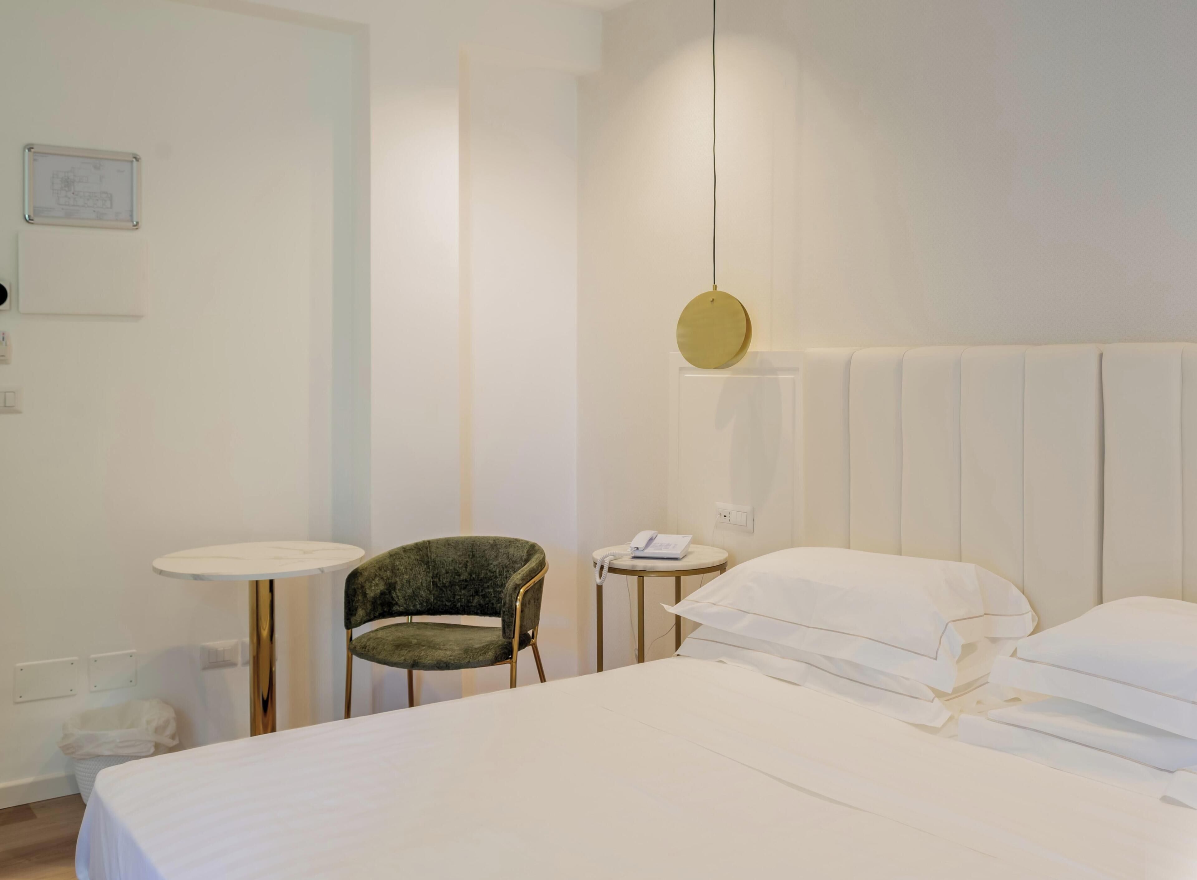 Ein Hotelzimmer mit einem Bett, einem Sessel, einem kleinen Tisch und einem Nachttisch mit Telefon.