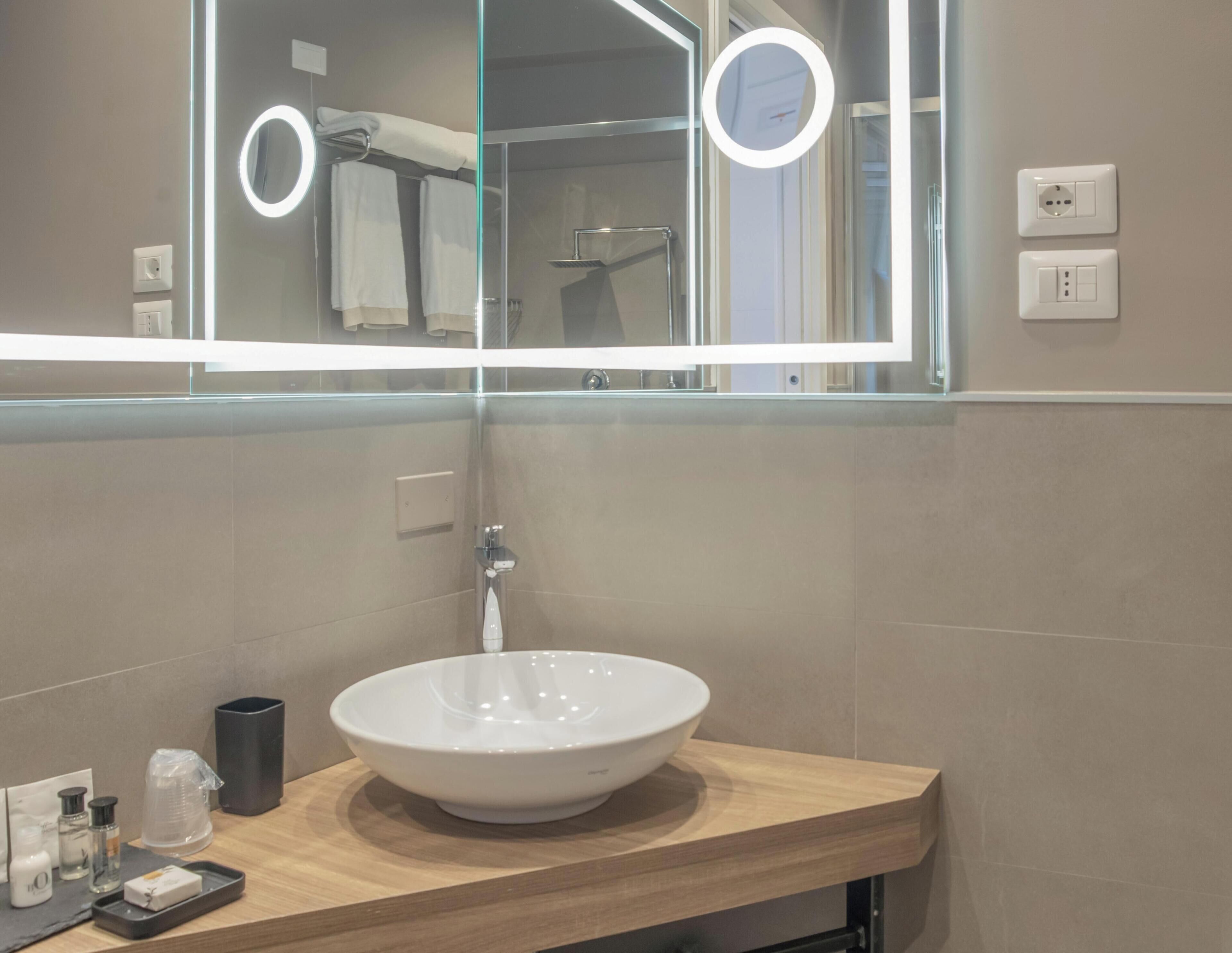 Un baño moderno con un espejo grande, un lavabo blanco y una encimera de madera.